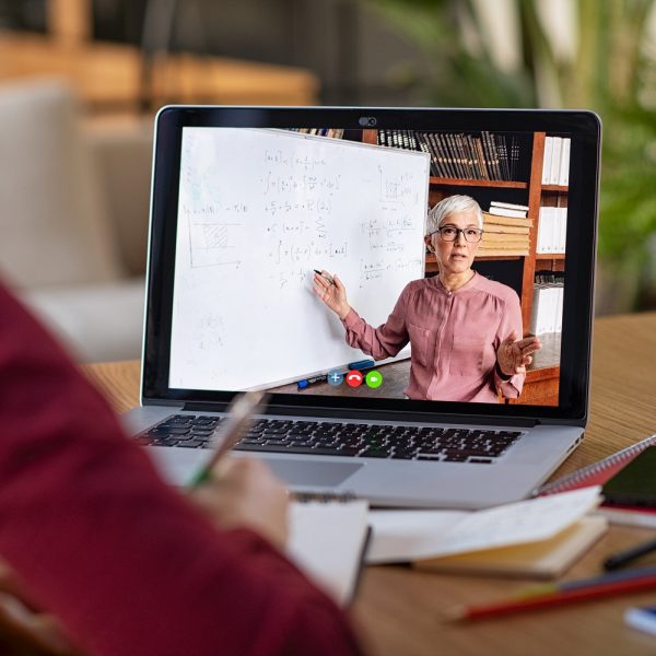 a person watching a lesson her laptop, featuring a lecturer demonstrating mathematical equations on a whiteboard