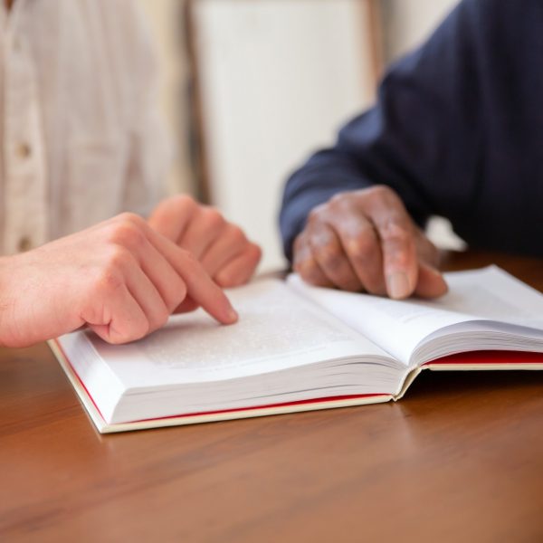 a person helping an older male read by pointing to spot in a book