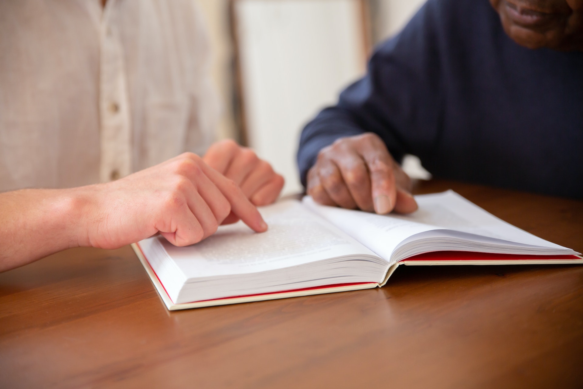 a person helping an older male read by pointing to spot in a book