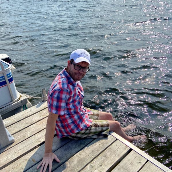 Troy dipping his feet in the lake while sitting on a pier