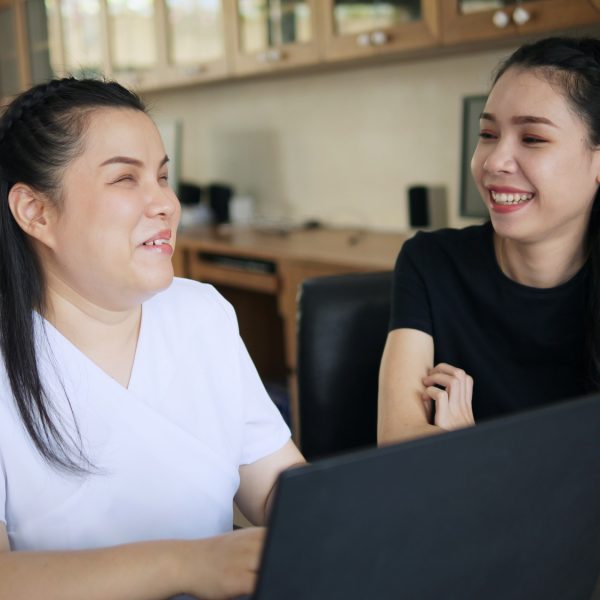 a woman and a blind woman smiling at each other as they work together on a laptop