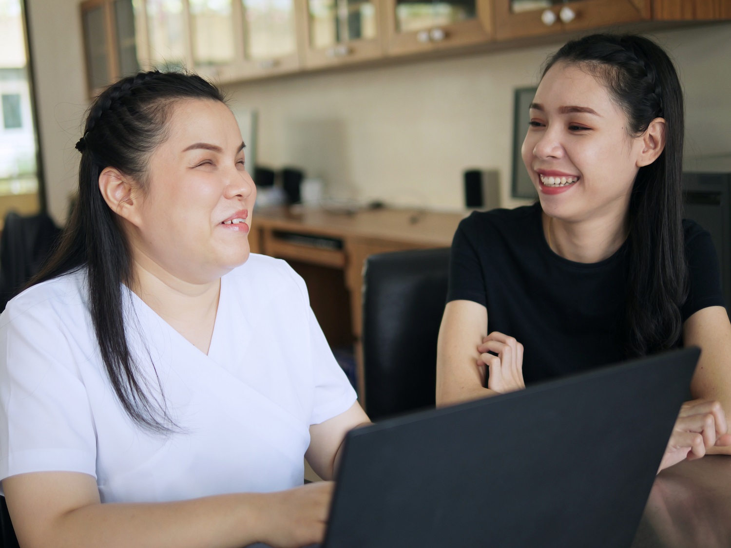 a woman and a blind woman smiling at each other as they work together on a laptop