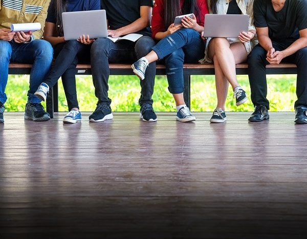 various people sitting on a bench using laptops and tablets