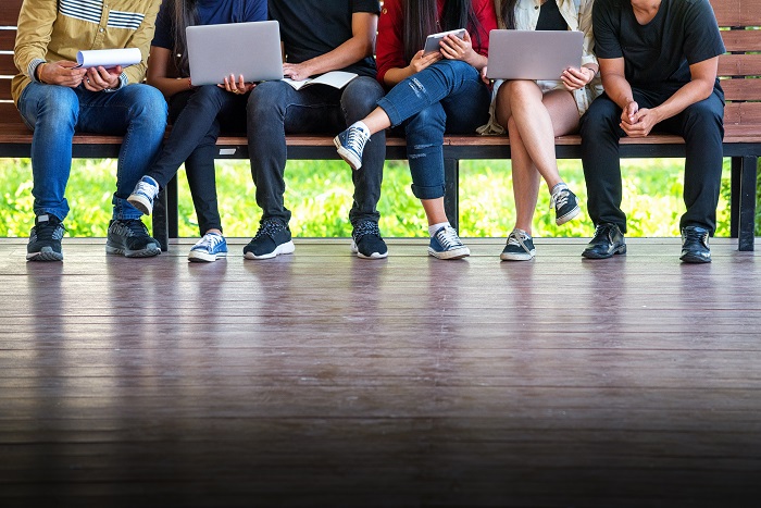 various people sitting on a bench using laptops and tablets