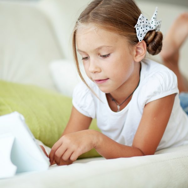 a young girl using a tablet on a couch