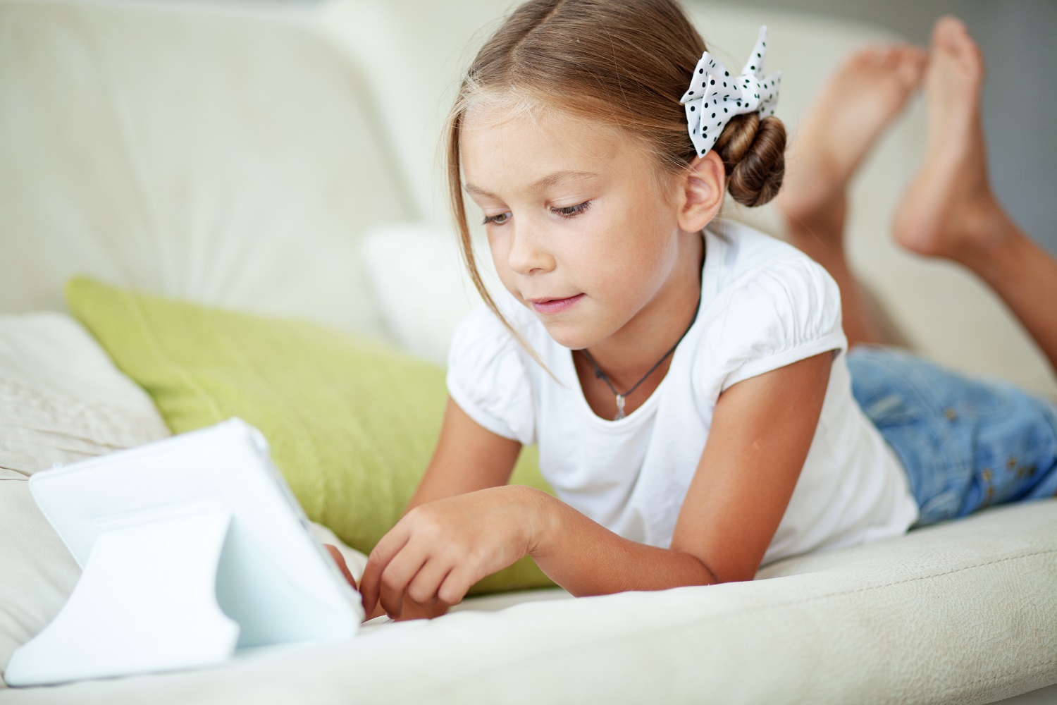 a young girl using a tablet on a couch