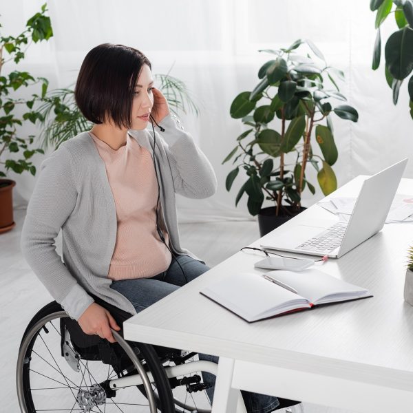 a woman in a wheelchair talking on a headset while using a laptop