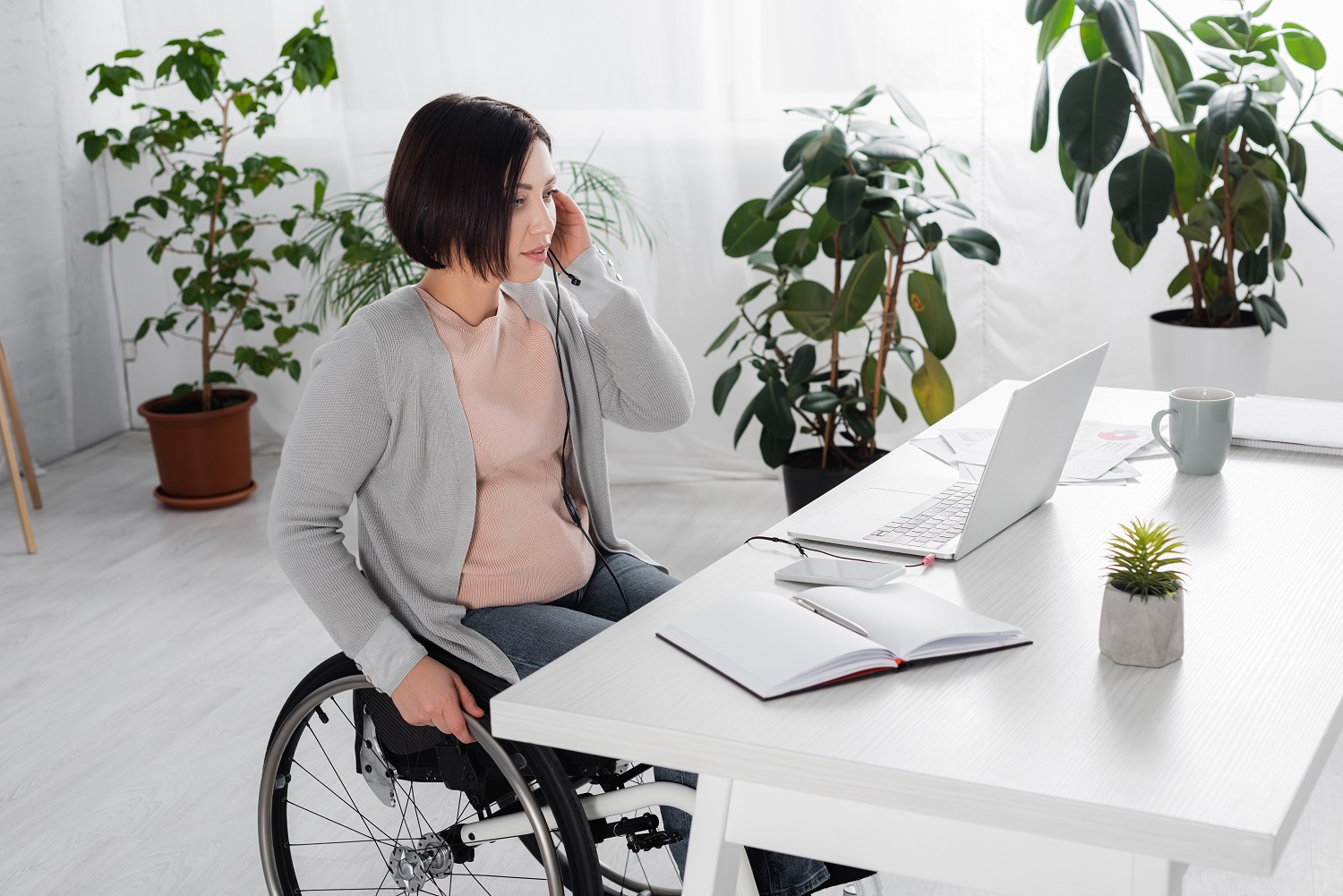 a woman in a wheelchair talking on a headset while using a laptop