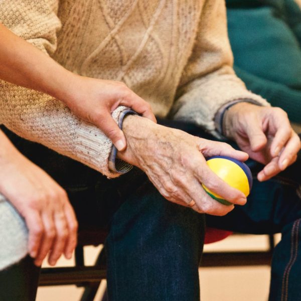 A caregiver holding a senior's hand, who is gripping a stress reliever ball.
