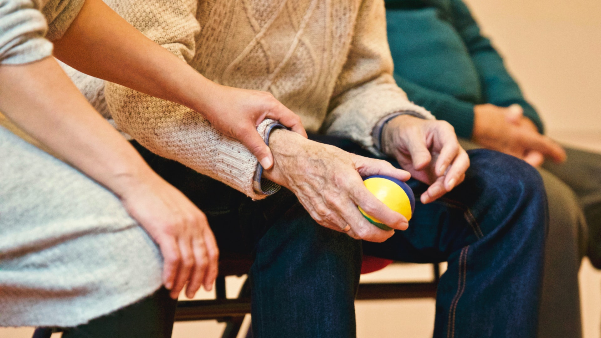 A caregiver holding a senior's hand, who is gripping a stress reliever ball.