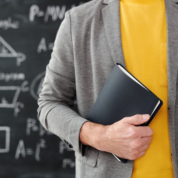 A teacher standing in front of a chalkboard holding a book.