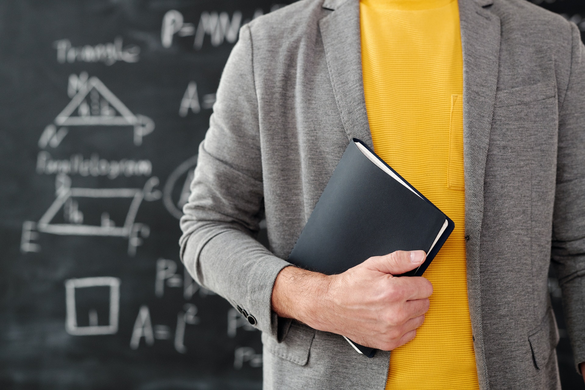 A teacher standing in front of a chalkboard holding a book.