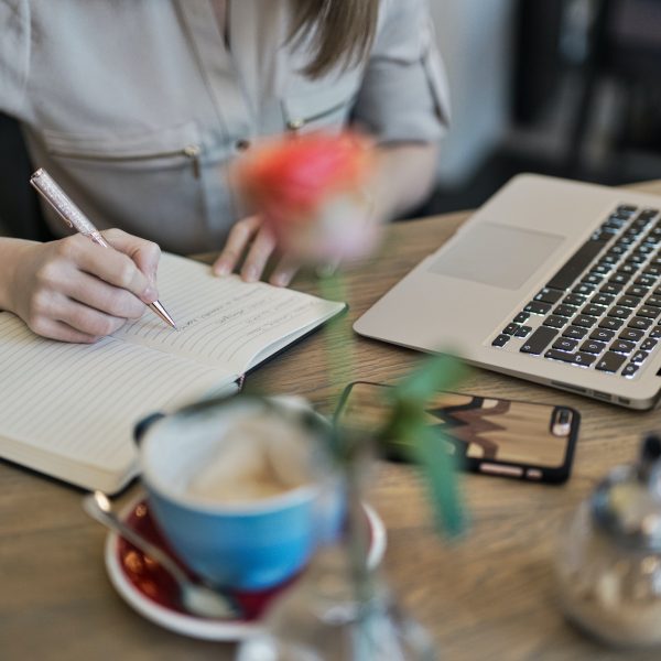 A woman writing on a notepad while using a laptop.