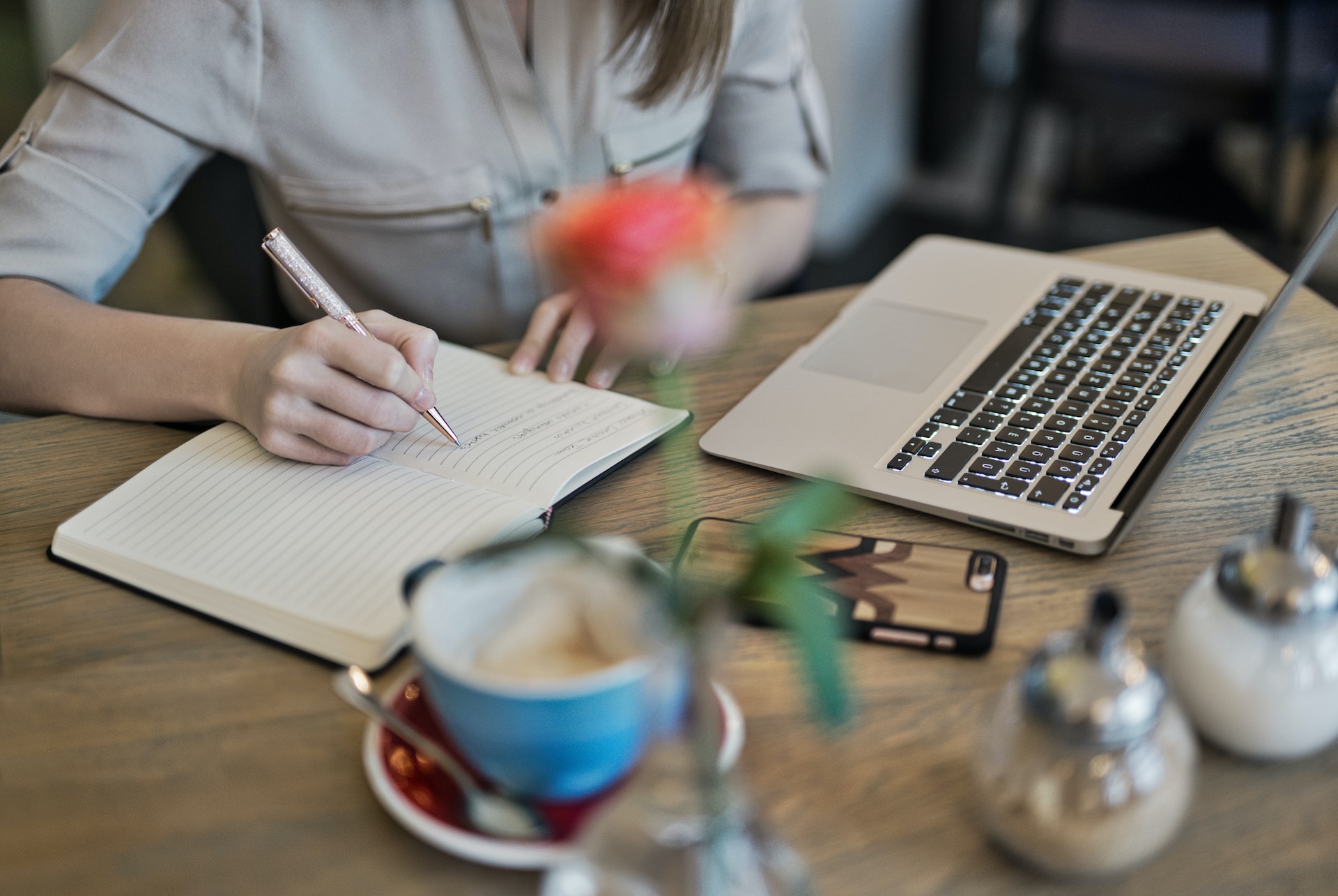 A woman writing on a notepad while using a laptop.