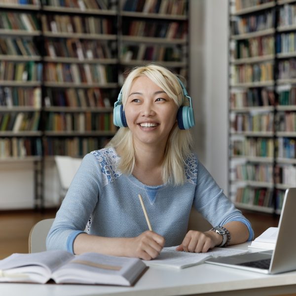 A female student wearing headphones writes in her notebook.