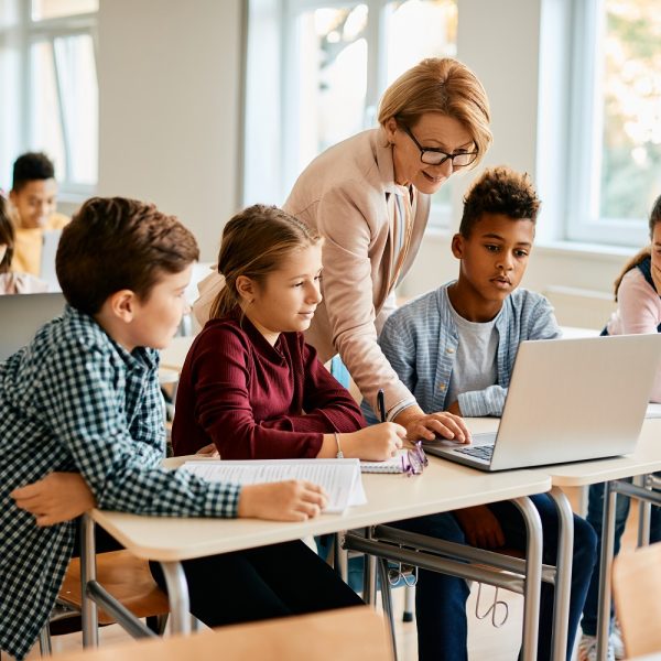 A teacher and her students using a laptop in a classroom.