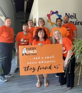 Our Regina staff wearing orange shirts and holding a sign that says, "Every Child Matters ...and a small voice whispers, they found us"