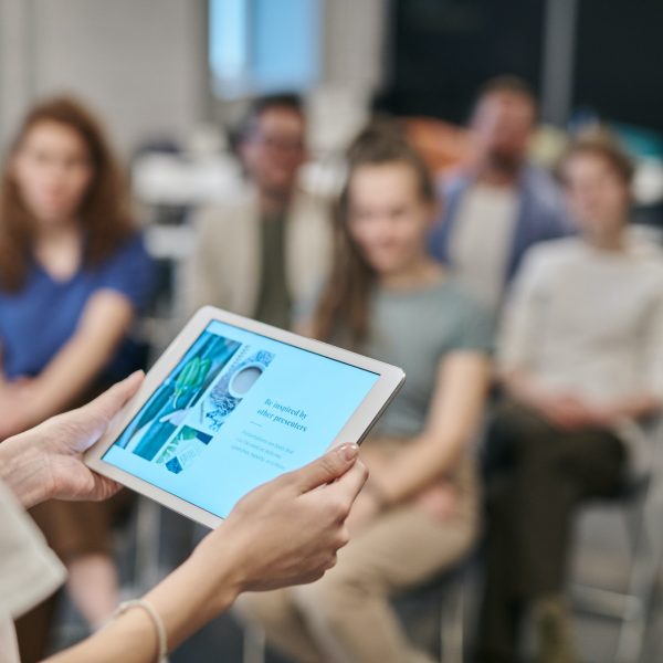 A teacher uses a tablet as she lectures to a class of adults.