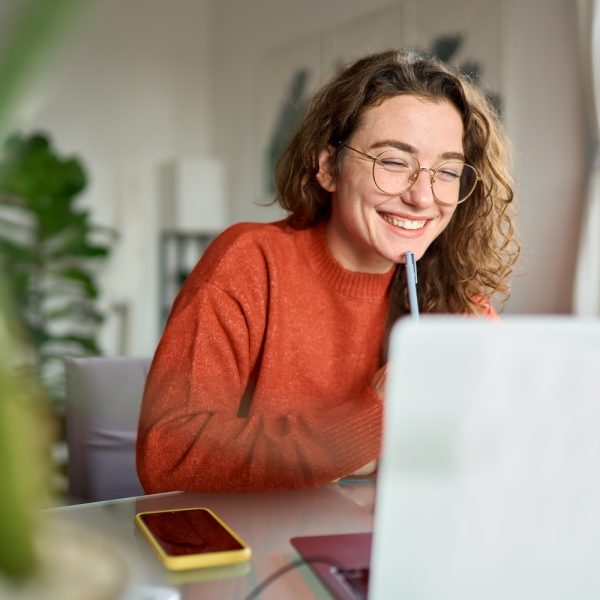 A woman uses a laptop, while writing down notes.