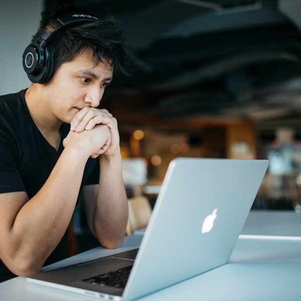 A man wearing headphones looks intently at his laptop.