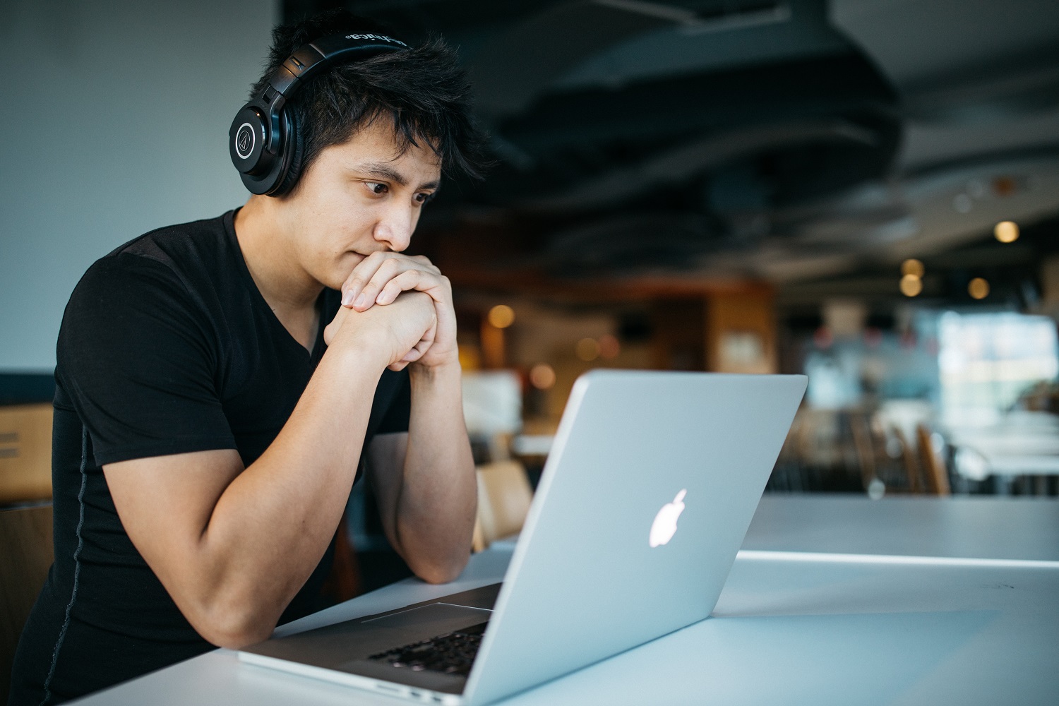 A man wearing headphones looks intently at his laptop.