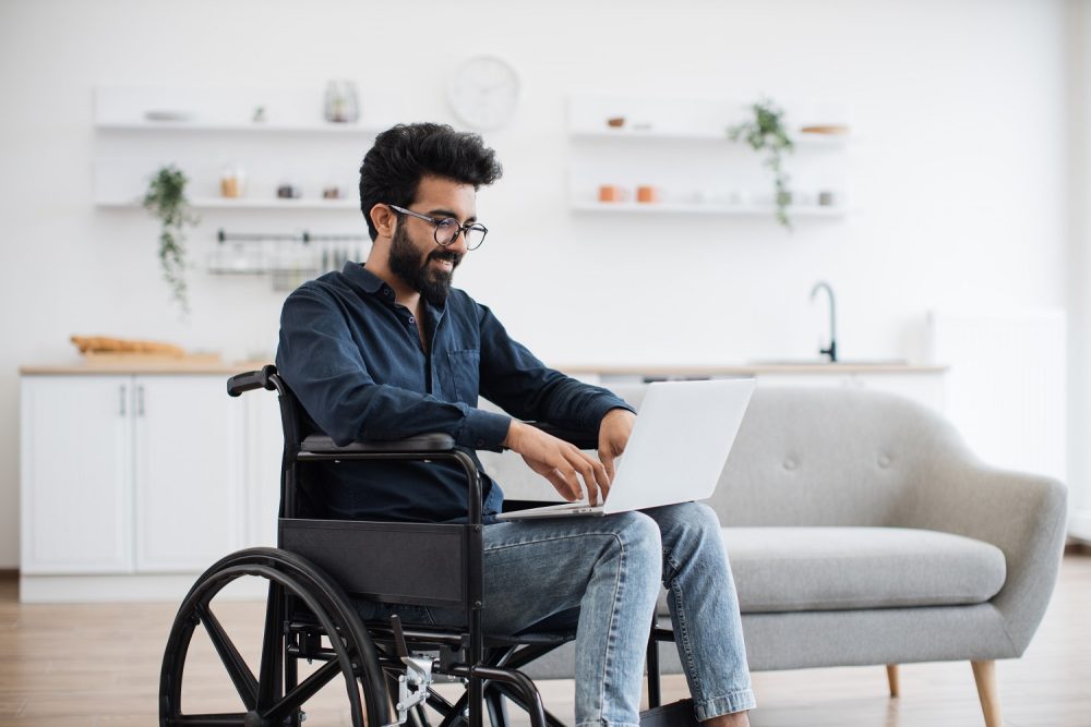 A man in a wheelchair uses a laptop.