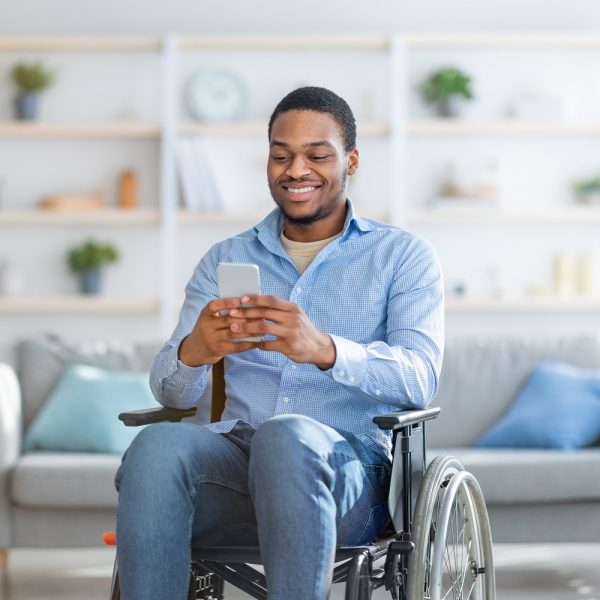 A man in a wheelchair smiles while he uses his phone.