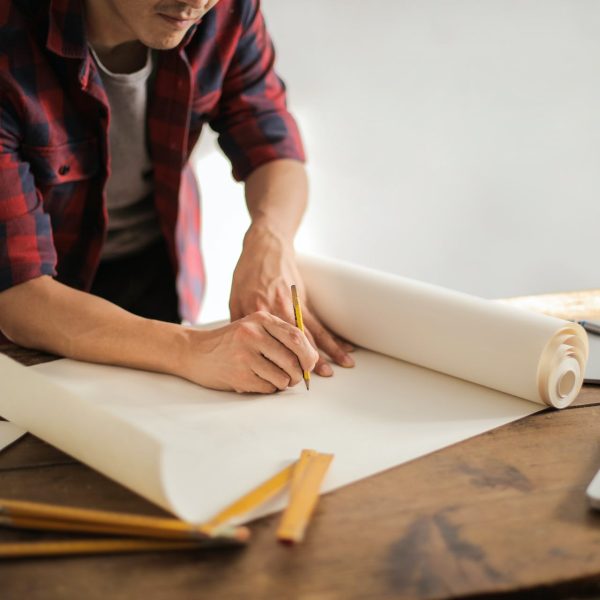 A man draws with a pencil on some plans.