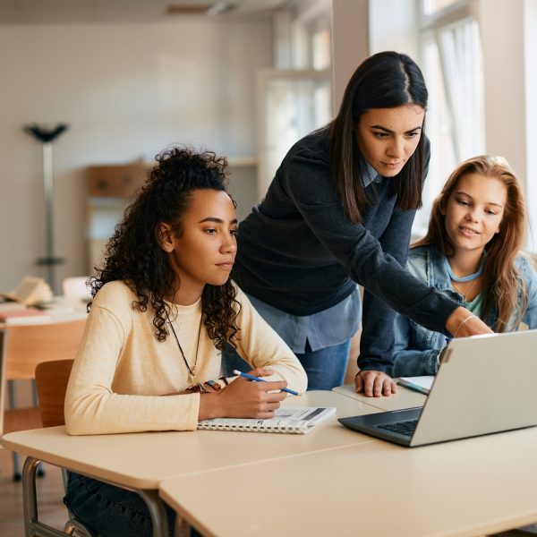 A high school teacher assisting her students in e-learning on a laptop in the classroom.