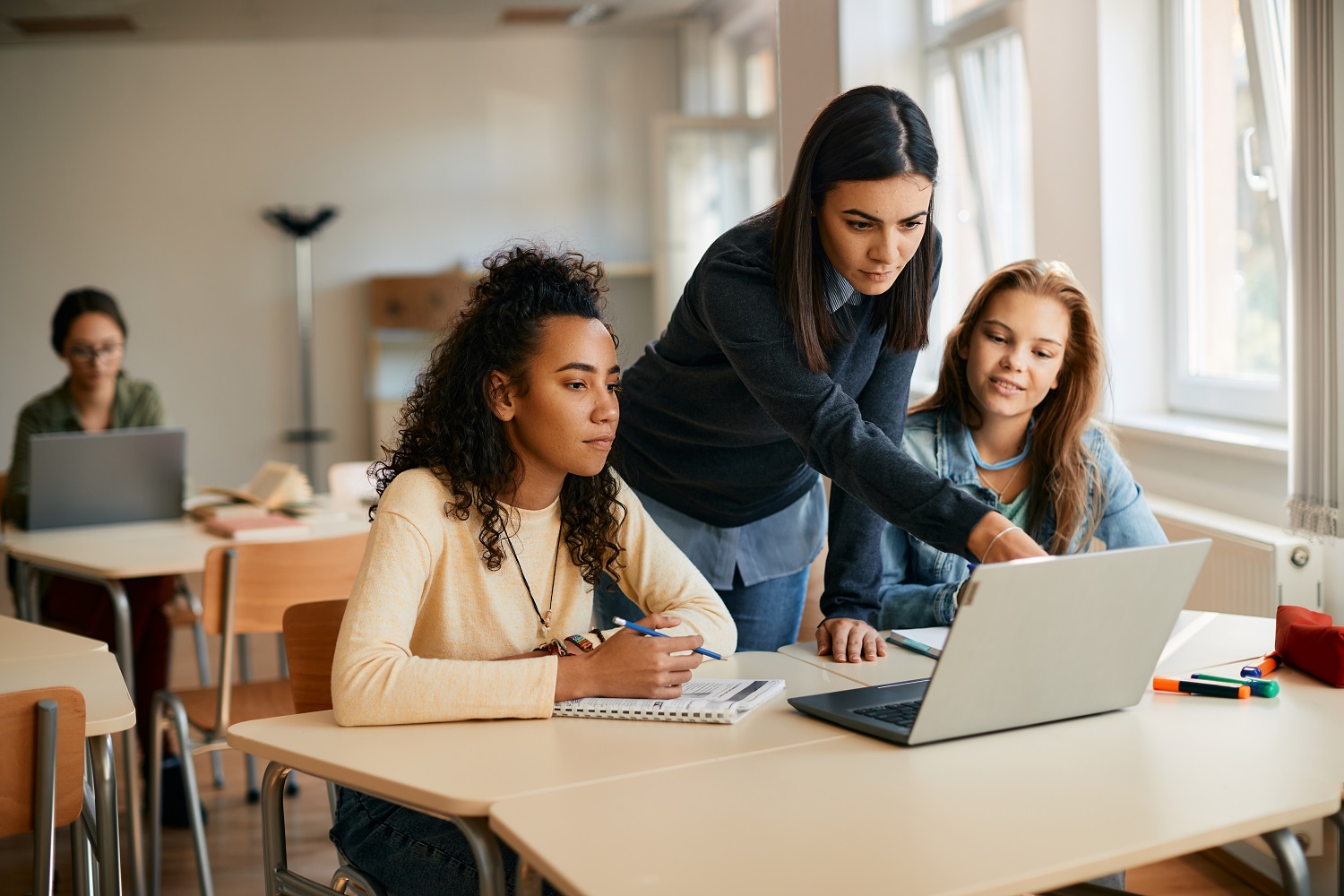 A high school teacher assisting her students in e-learning on a laptop in the classroom.