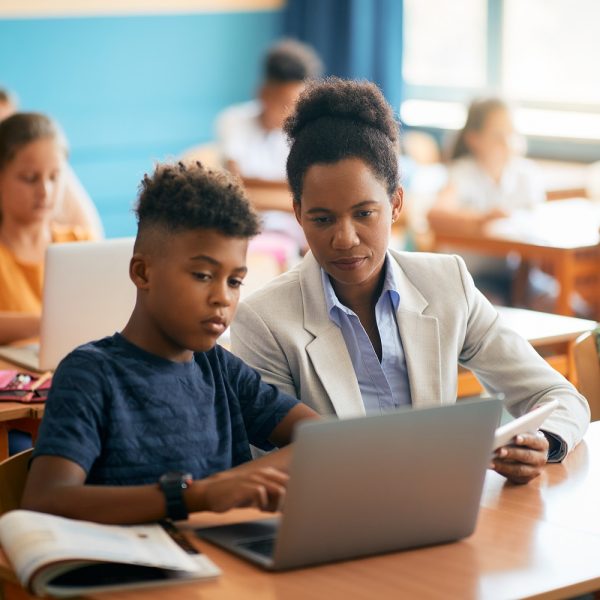 A teacher assisting a student in using a laptop during class.