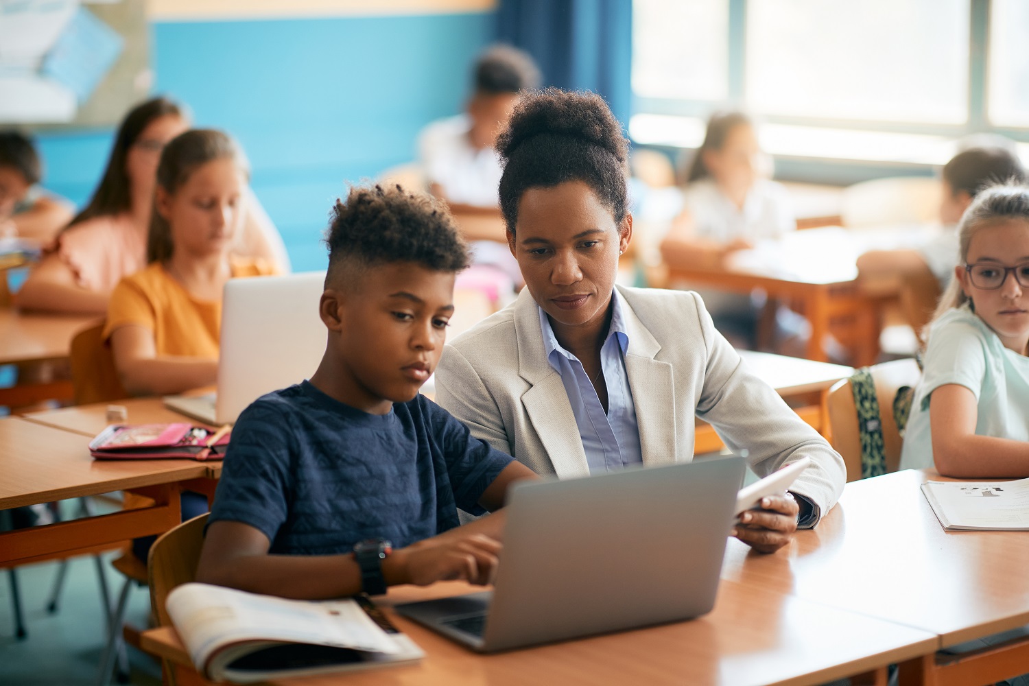 A teacher assisting a student in using a laptop during class.