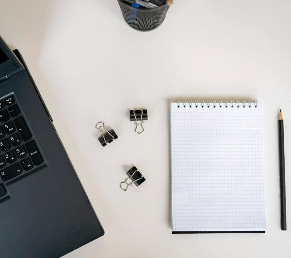 A pad of graphing paper next to a pencil, paper clips, and a laptop.