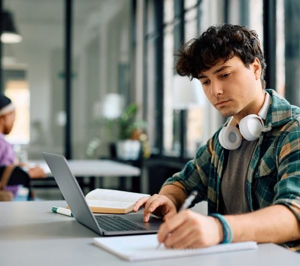A student takes notes while going on a laptop.