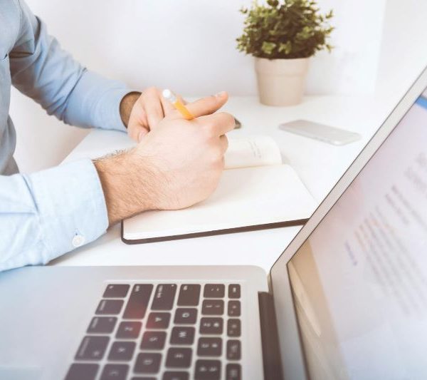 A man writes into a notebook while going on a laptop.