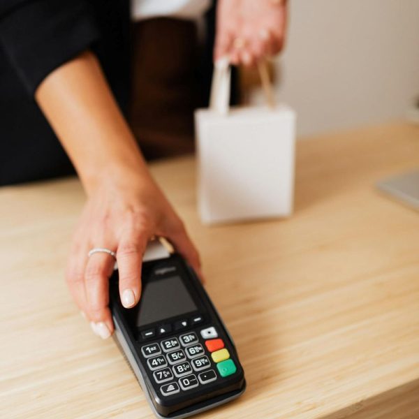 A cashier hands over a payment terminal, while holding a small bag.