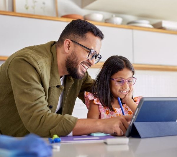 An adult male helps a young girl using a tablet.