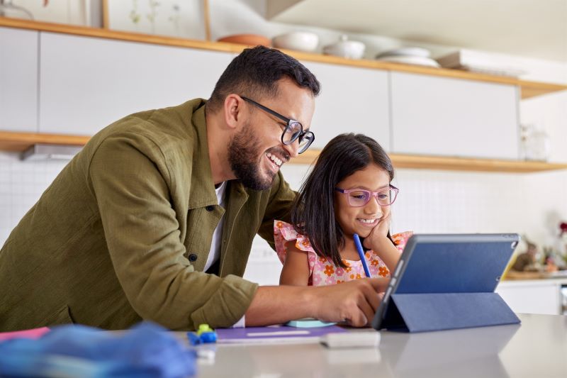 An adult male helps a young girl using a tablet.