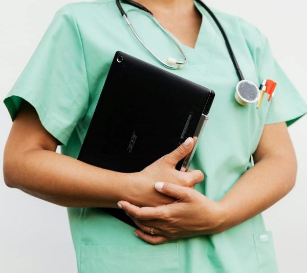 A nurse wearing scrubs and a stethoscope carries a file.