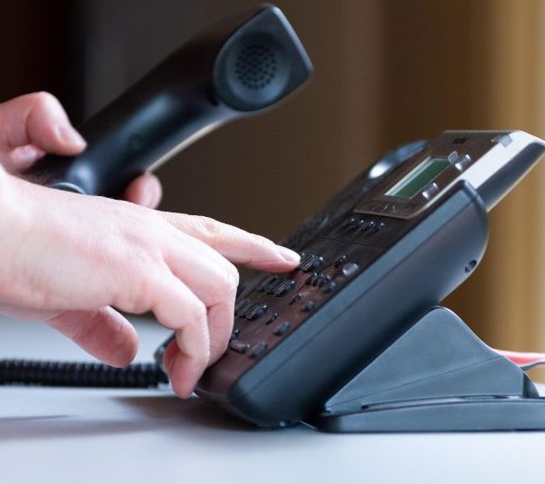 A person dialing a number on a landline phone.