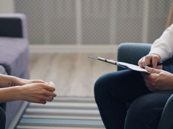 A counselor holds a clipboard and talks to a client.