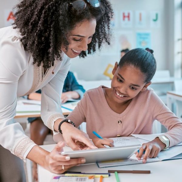 A teacher helps a student using a tablet.