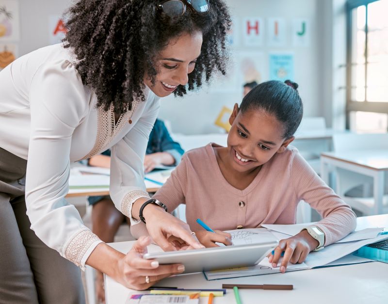 A teacher helps a student using a tablet.