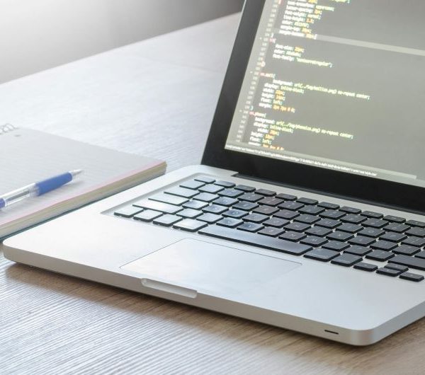 A laptop being used for coding, with a notebook and pen beside it.