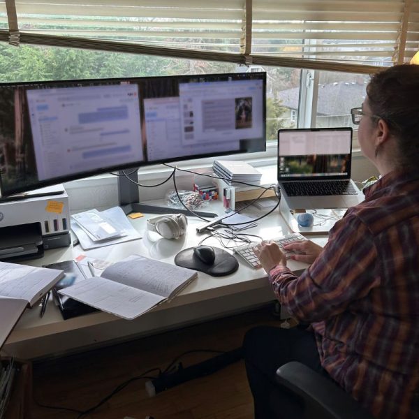 Debbie at her workstation, using a large curved monitor in addition to her laptop.