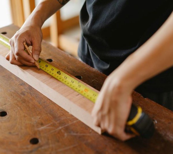 A person measures a board of wood with a tape measurer.