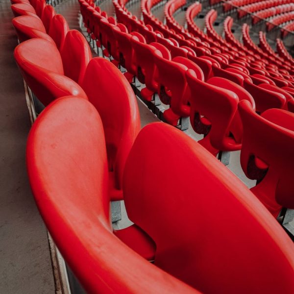 Curved rows of empty bright red stadium seats stretching into the distance in a large arena.