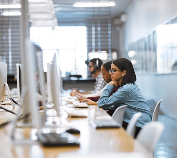 Students working on computers in a modern library with rows of desktop computers and bookshelves.