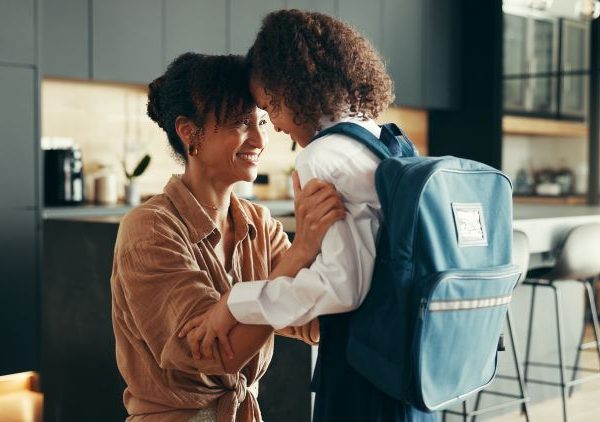 Mother and daughter sharing a joyful moment in a modern kitchen as the child prepares to leave for school with a blue backpack.
